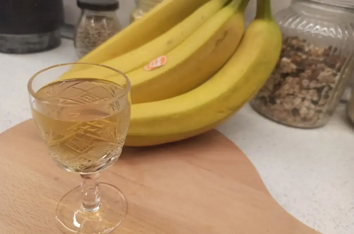 Szklaneczka z nalewką z banana, obok pęk żółtych bananów.