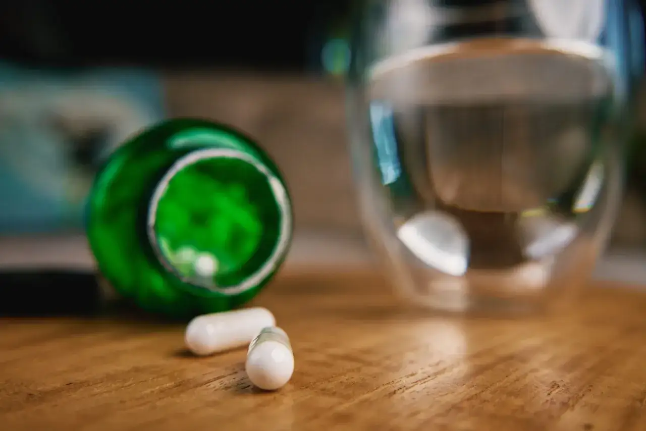 Kapsułki z berberyną obok szklanki wody. Czy berberyna a alkohol to dobre połączenie?