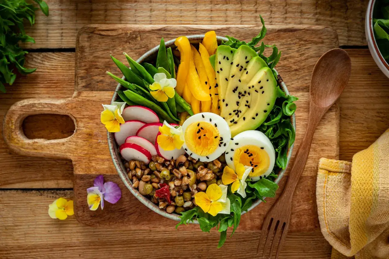 Kolorowa buddha bowl z jajkiem, awokado, rzodkiewką, fasolką i kwiatami. Zdrowy posiłek pełen witamin.