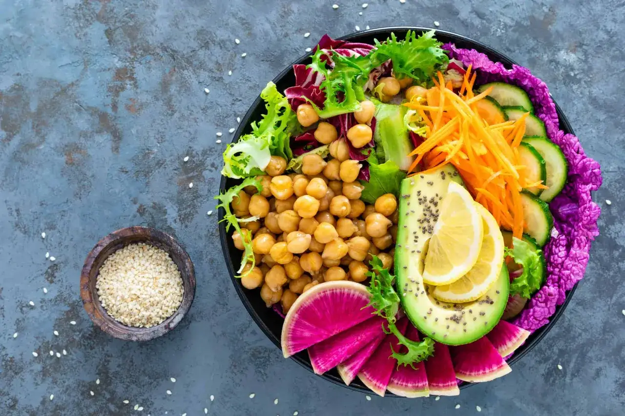 Kolorowa buddha bowl z ciecierzycą, awokado, rzodkiewką, ogórkiem, marchewką i sałatą.