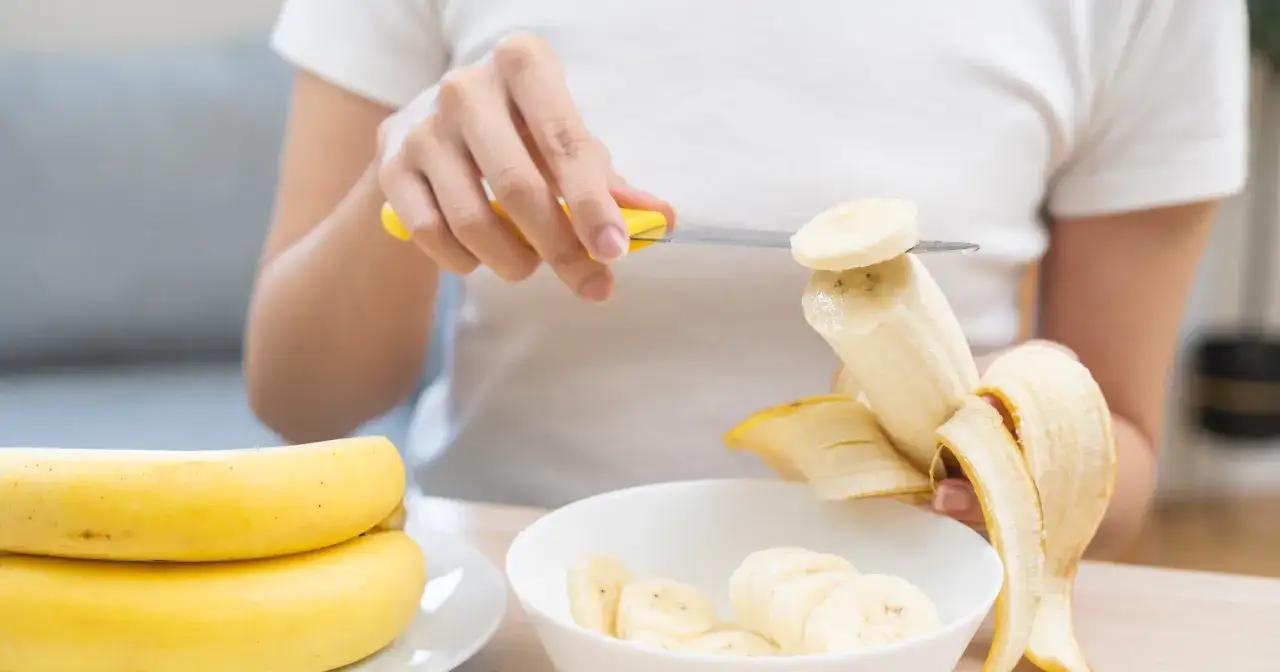 Kobieta kroi banana na plasterki, przygotowując zdrowy posiłek. Zastanawiasz się, ile bananów dziennie to optymalna ilość?