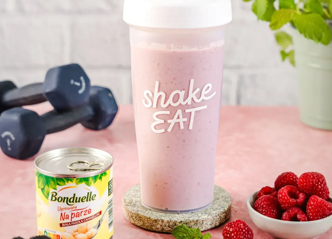 Idealny posiłek przed treningiem: różowy shake, maliny, puszka fasoli i hantle.
