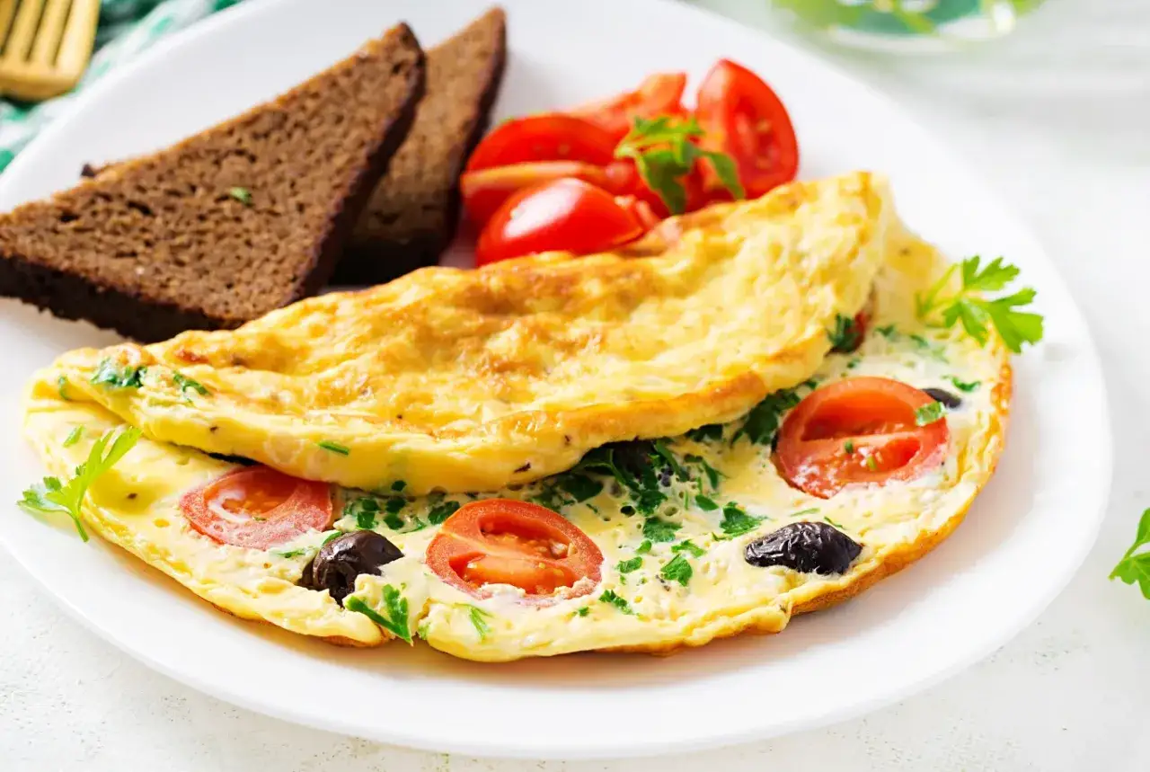 Pyszna, zdrowa kolacja: omlet z pomidorami i oliwkami, podany z ciemnym pieczywem i świeżą natką pietruszki.
