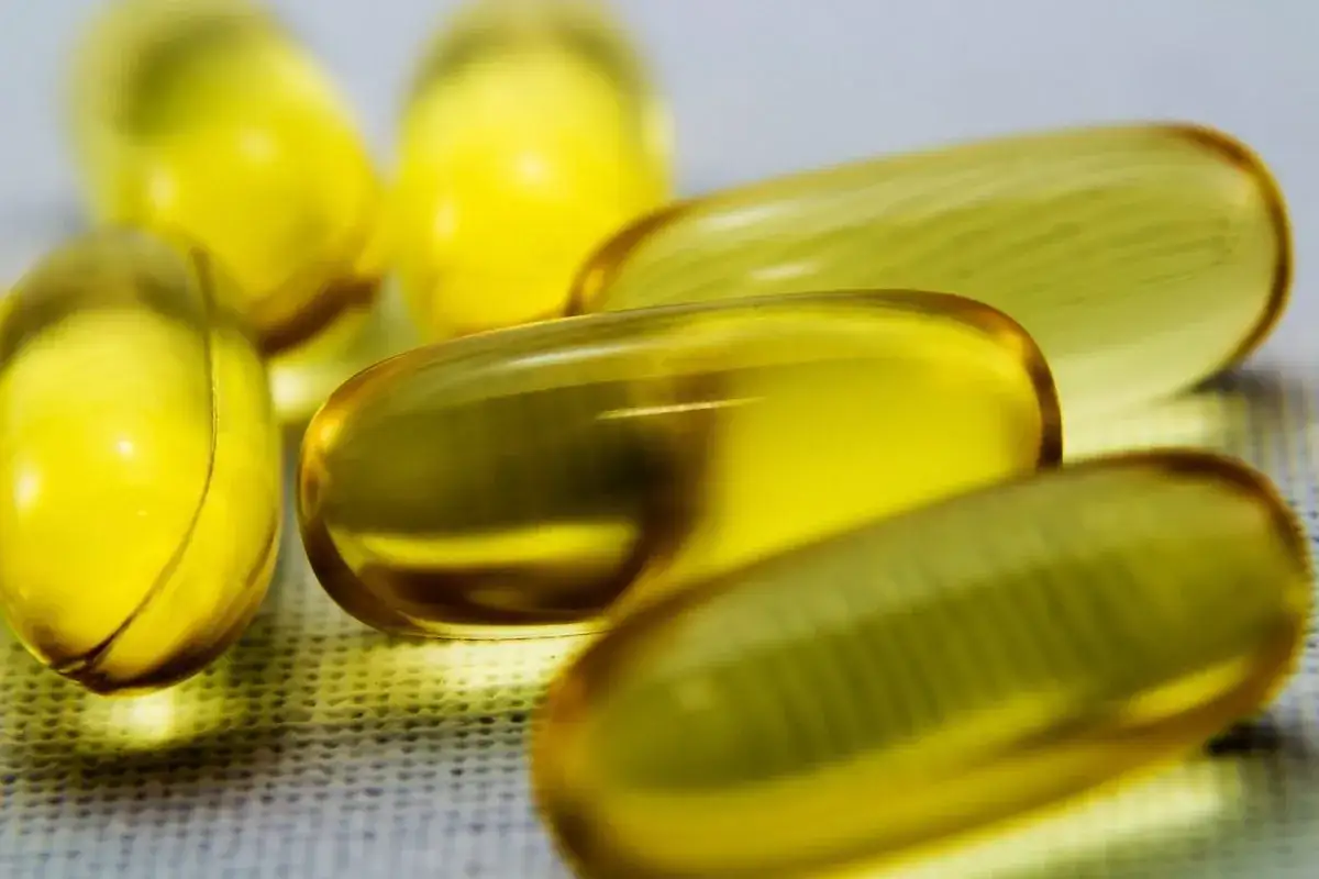 Żółte kapsułki omega 3 leżą na białej powierzchni. Uważaj na przedawkowanie omega 3, bo może być niebezpieczne.