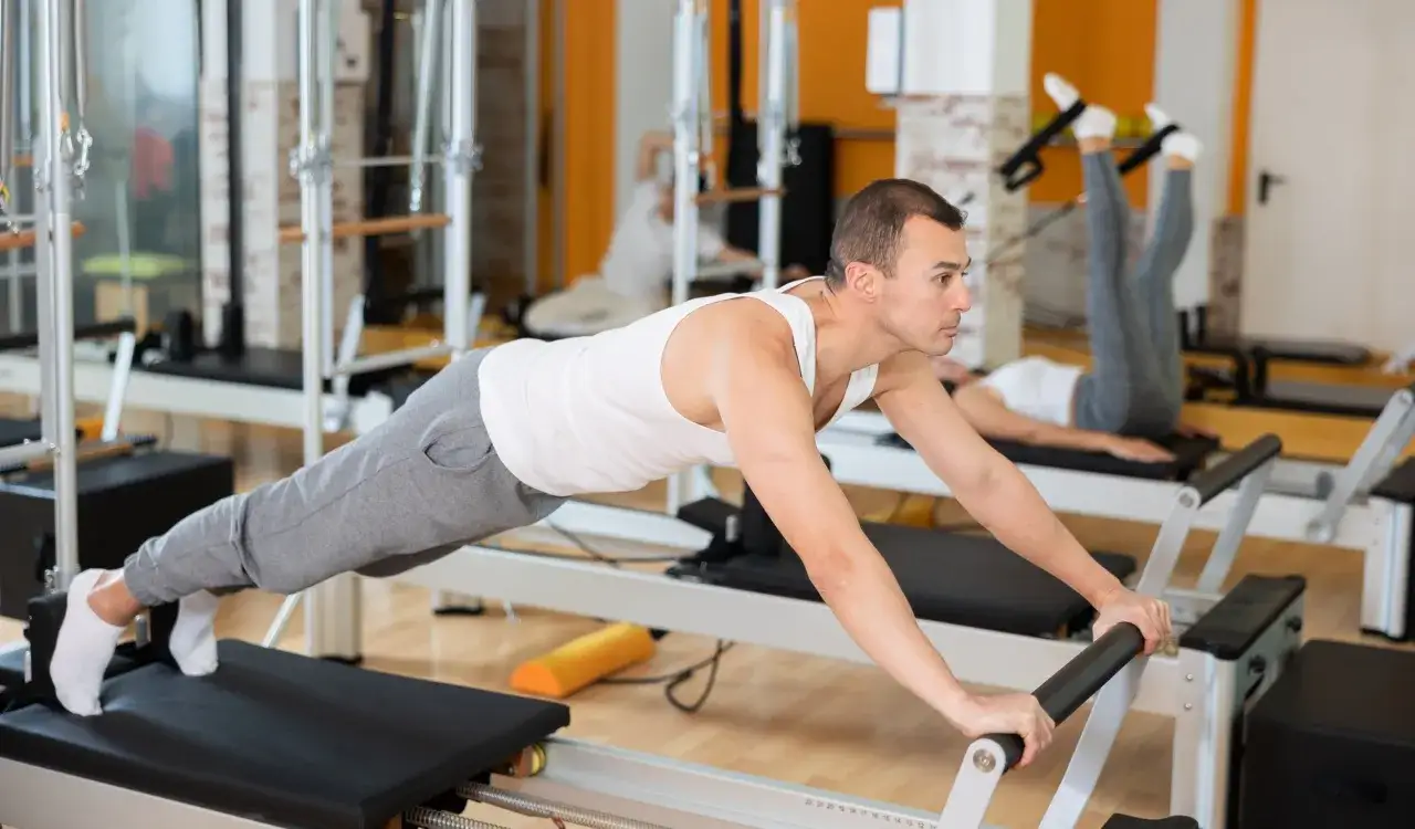 Mężczyzna i kobieta ćwiczą na reformerach. Czy pilates odchudza? Tak, regularne ćwiczenia wzmacniają ciało i mogą pomóc w redukcji wagi.
