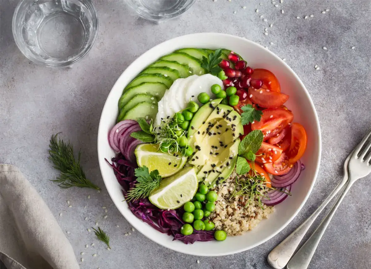 Kolorowa buddha bowl z awokado, pomidorami, ogórkiem, czerwoną cebulą, groszkiem, granatem i komosą ryżową.