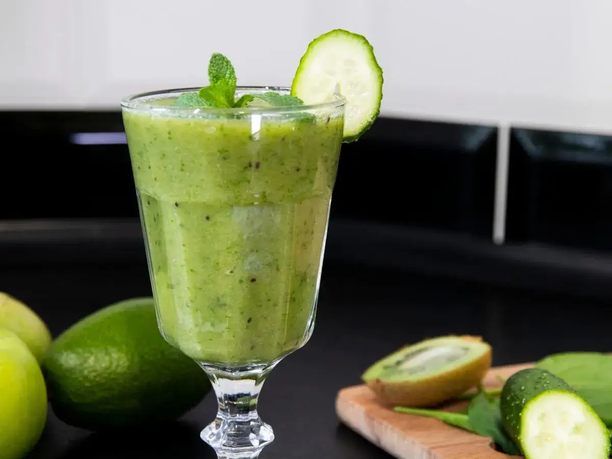 Zielony koktajl z miętą i plasterkiem ogórka, obok jabłka, limonki i kiwi. Idealny na zdrowe koktajle sirt przepisy.