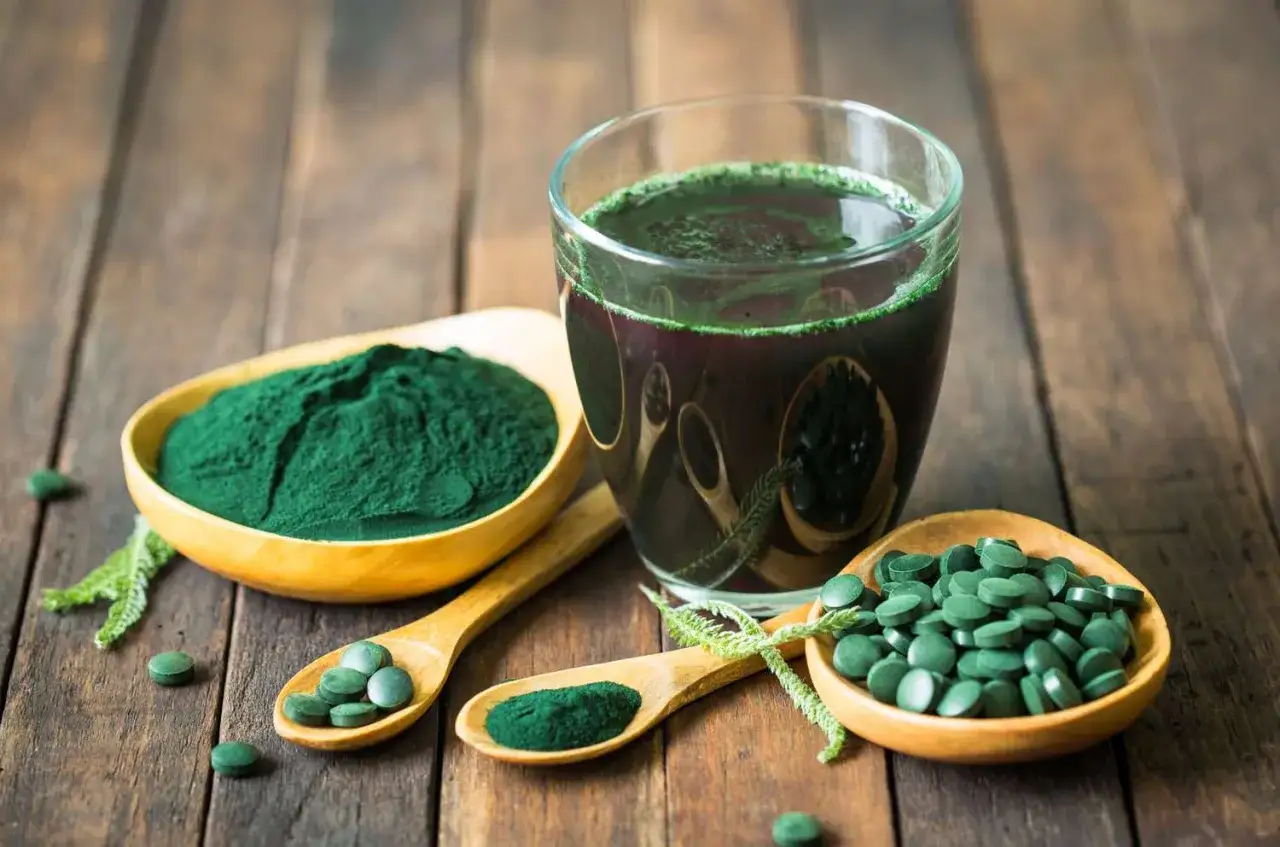 Chlorella vs spirulina: zielony proszek, tabletki i napój na drewnianym tle.