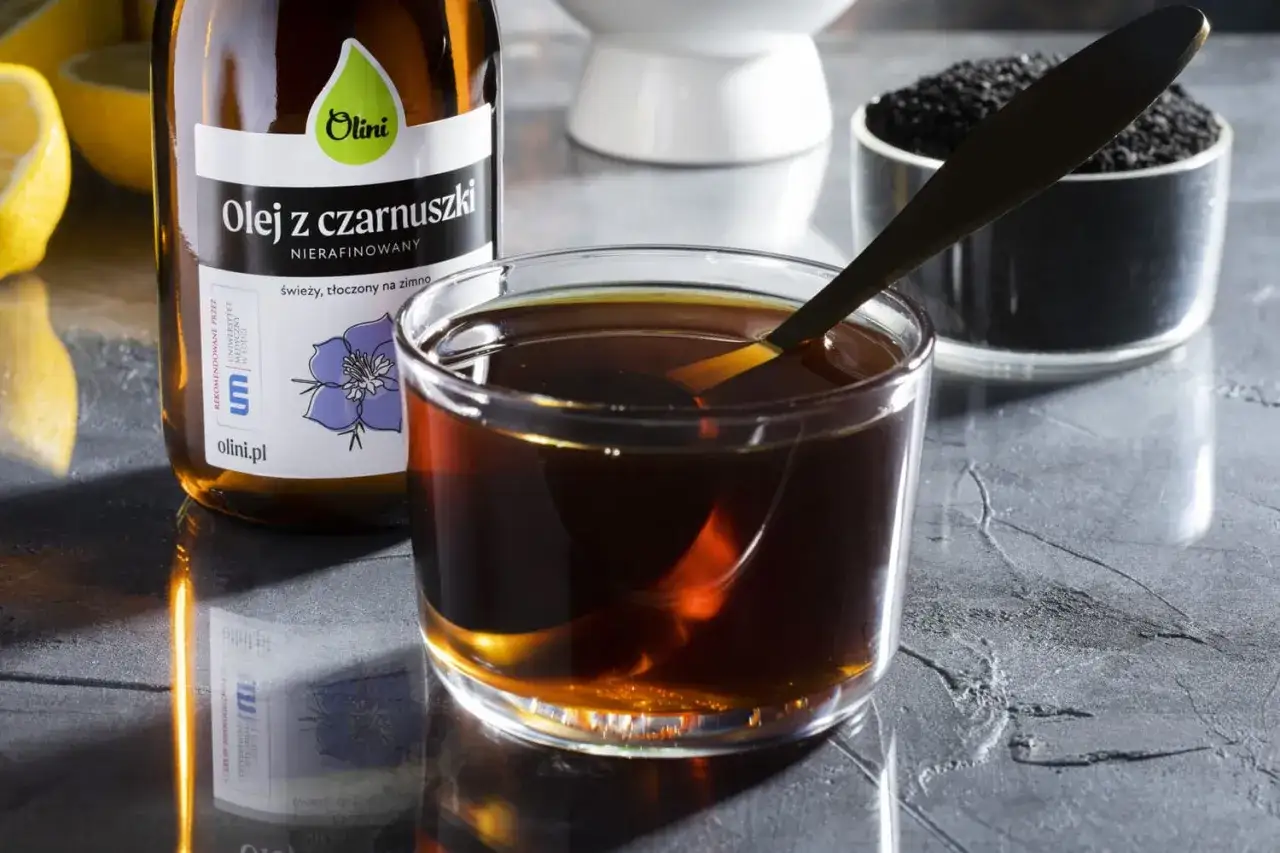 Ciemny, aromatyczny syrop z czarnuszki w szklance, obok butelki oleju i nasion. Idealny na zdrowie!