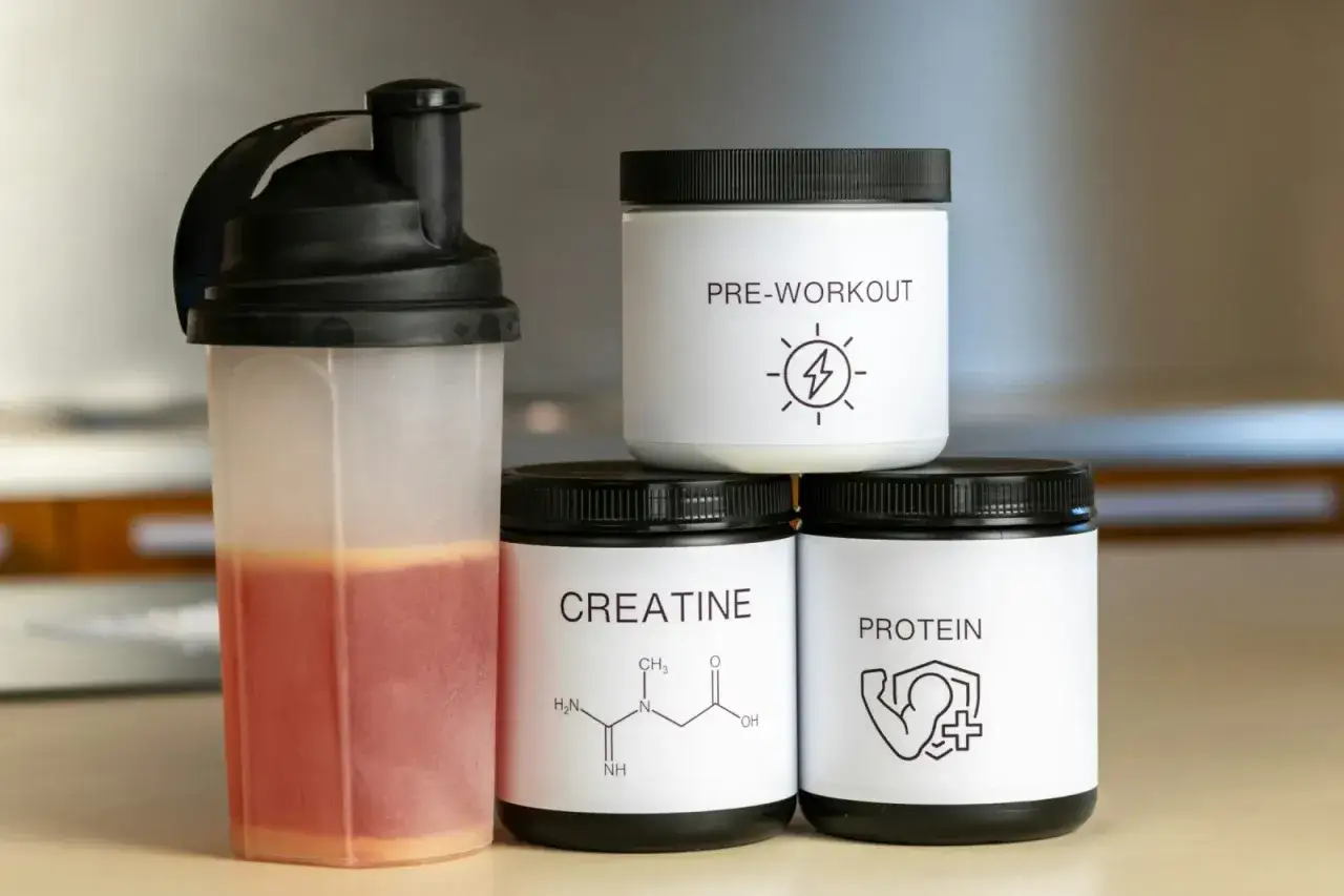 Shaker z napojem i puszki z odżywkami: kreatyna, pre-workout, protein. Wybór między kreatyną jabłczan czy monohydrat?