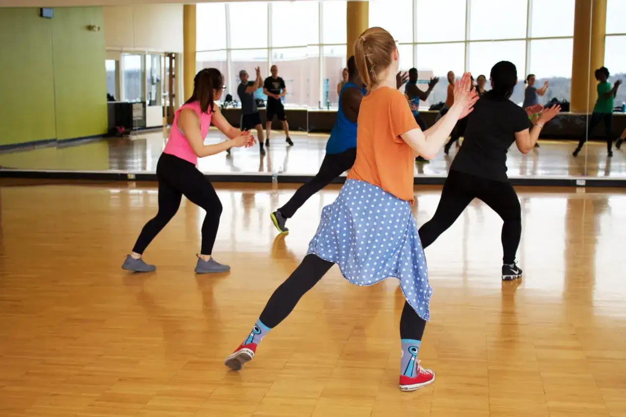 Grupa osób ćwiczy zumbę w sali z lustrami. Radosna atmosfera i ruch to esencja tego, co to jest zumba.