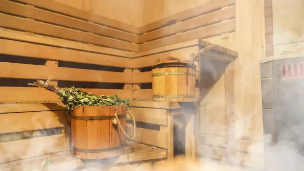 Drewniana sauna po siłowni, z parującym wiadrem i miotełką. Idealne miejsce na relaks i regenerację.