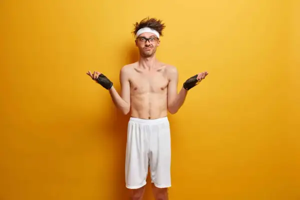 Chudy mężczyzna w rękawiczkach treningowych i opasce na głowie rozkłada ręce, jakby pytał "ektomorfik co to?".