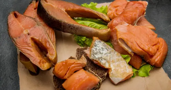 Kawałki wędzonego łososia na liściach sałaty i ciemnym pieczywie. Czy łosoś wędzony jest zdrowy? Tak, to bogactwo kwasów omega-3.