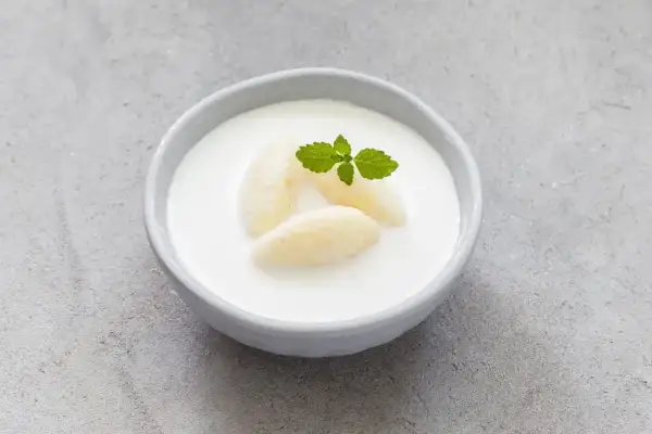Kogel-mogel czy jest zdrowy? Miseczka z deserem z bitej śmietany, kawałkami banana i listkiem mięty.