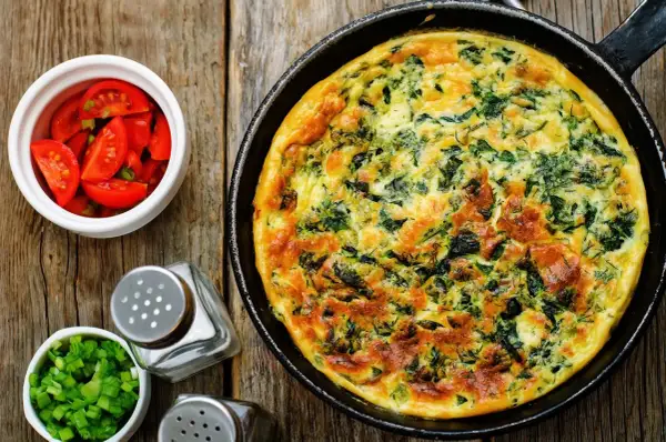 Frittata ze szpinakiem i serem, idealna jako pomysł, czym zastąpić węglowodany. Obok pomidorki i szczypiorek.