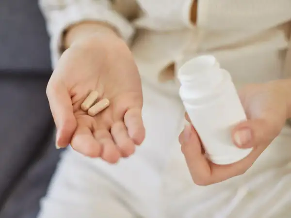 Dwie kapsułki na dłoni i biały pojemnik. Zastanawiasz się, colostrum na co? To naturalne wsparcie dla odporności.