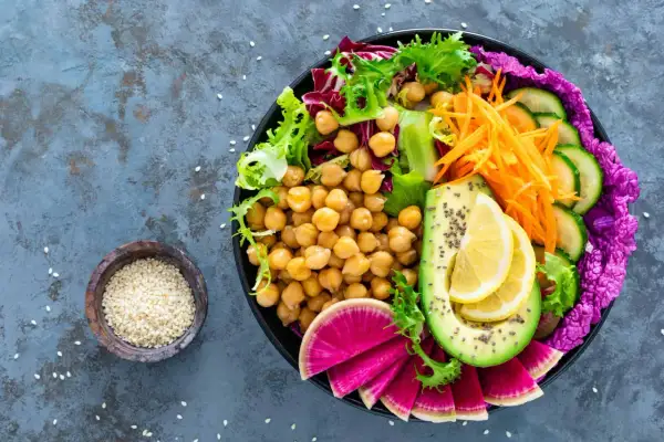 Kolorowa buddha bowl z ciecierzycą, awokado, rzodkiewką, ogórkiem, marchewką i sałatą.