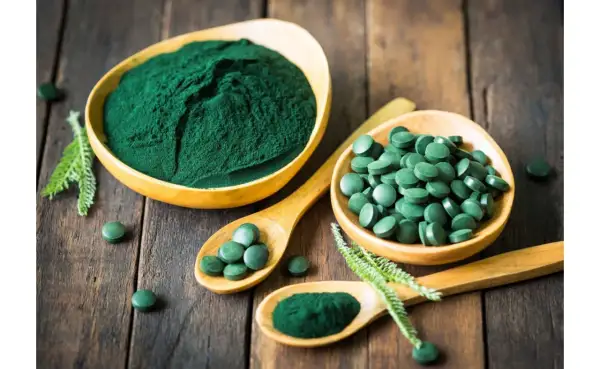 Chlorella vs spirulina: zielony proszek i tabletki na drewnianym tle. Dwa rodzaje alg w formie suplementów diety.