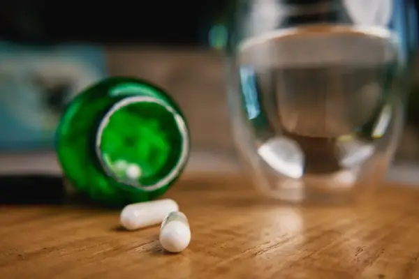Kapsułki z berberyną obok szklanki wody. Czy berberyna a alkohol to dobre połączenie?