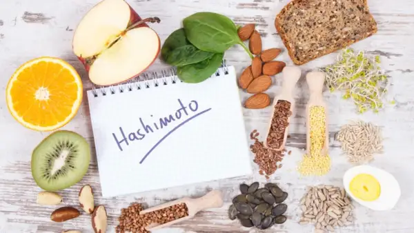 Zdrowe produkty i notatnik z napisem "Hashimoto". Rozważ jakie suplementy przy niedoczynności tarczycy mogą pomóc.