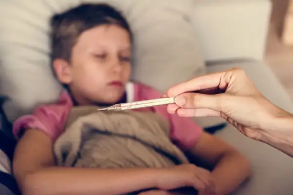 Dziecko 10 lat leży chore, ma zimne ręce. Mama mierzy mu temperaturę.
