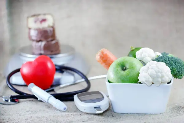 Zdrowe jedzenie, jak jabłko i warzywa, wspiera dietę mitochondrialną. Obok serce, stetoskop i glukometr symbolizują troskę o zdrowie.