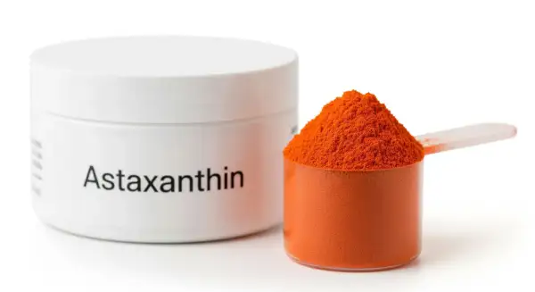 Słoiczek z napisem "Astaxanthin" i miarka pełna pomarańczowego proszku. Poznaj astaksantyna działanie!
