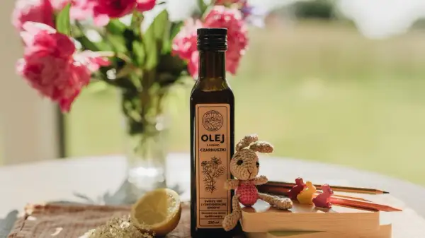 Olej z czarnuszki w butelce, obok cytryny, kwiatów i szydełkowego zajączka. Od jakiego wieku można go stosować?